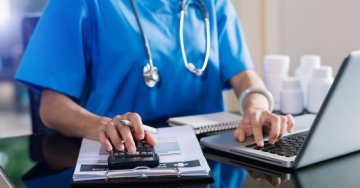 Doctor working at a computer and using a calculator on a table