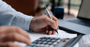 man writing while using a calculator