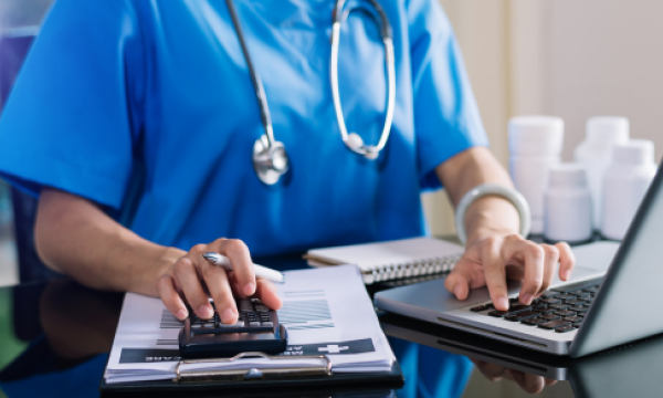 Doctor working at a computer and using a calculator on a table