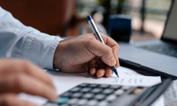 man writing while using a calculator