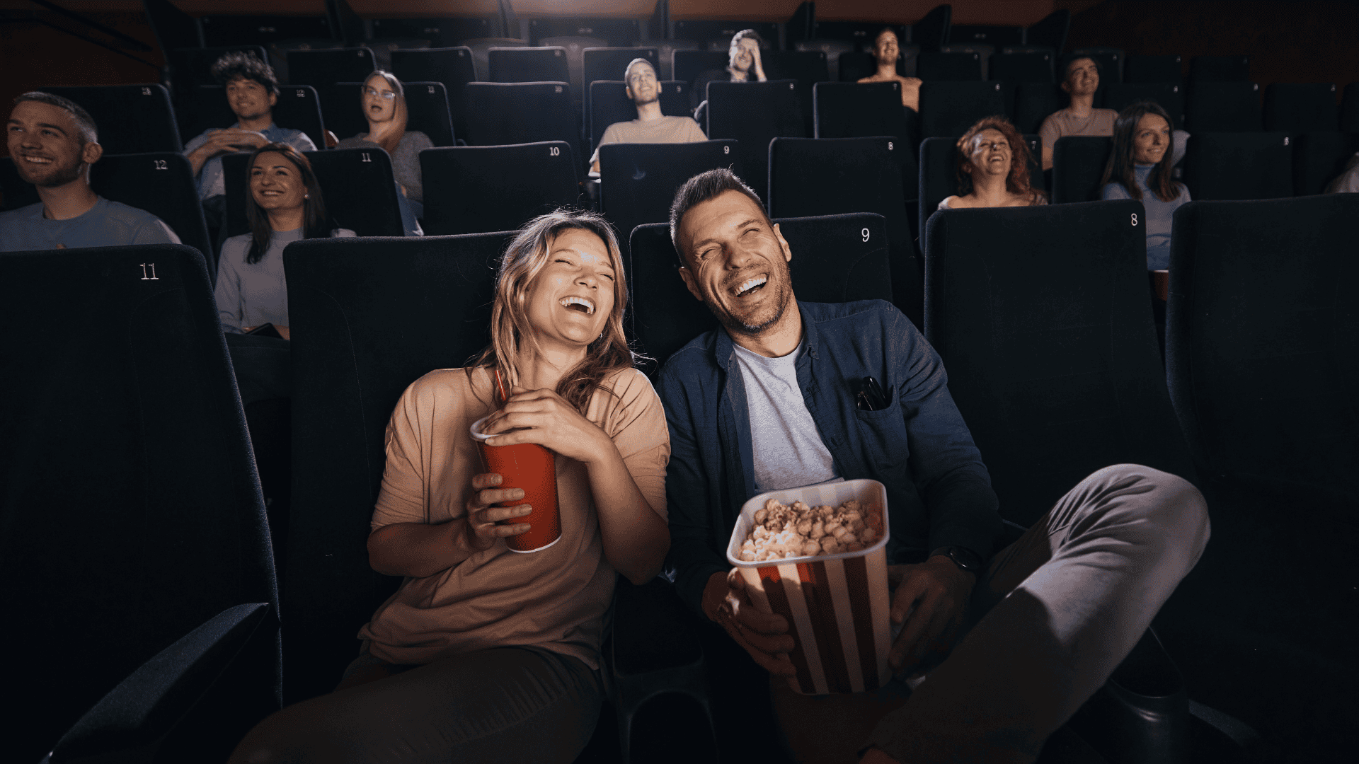 Happy couple watching a romantic comedy at the cinema with popcorn and drinks.