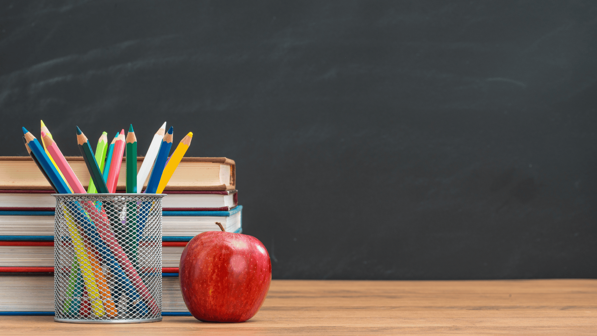 Books stacked on a desk with pencils and an apple
