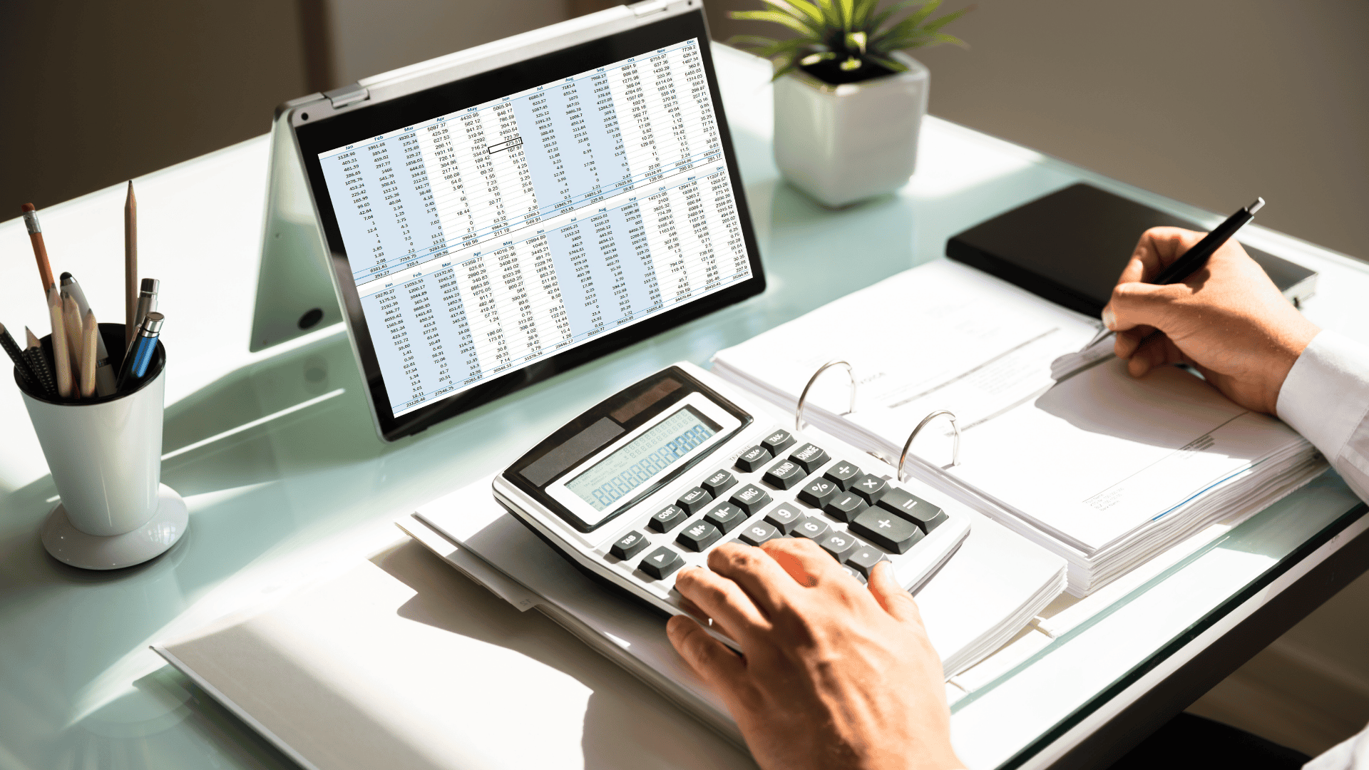 Hands on a calculator and holding a pen.